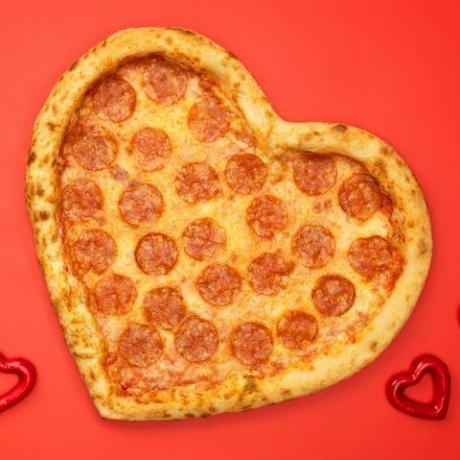 بيبروني بيتزا على شكل قلب ليوم عيد الحب على خلفية ورقة حمراء